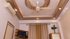 A room with a ceiling fan, recessed lighting, a mounted air conditioner, a flat-screen TV, and a curtain. - Hotel Buddha International (Patna)