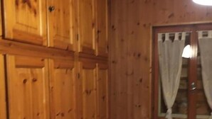 A room with wooden paneling, a window with curtains, a radiator, and a bed with a patterned bedspread. - 2-bedroom apartment (Bosco Chiesanuova)