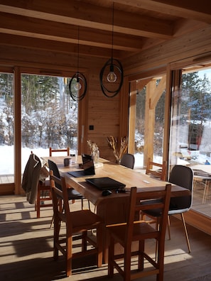 A wooden interior with a large dining table, chairs, and hanging light fixtures.