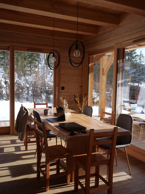 A wooden interior with a large dining table, chairs, and hanging light fixtures.