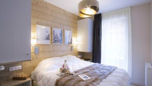 Et hotelværelse med en stor seng, et træhovedgærde, billedkunst på væggen, et natbord med lampe og et vindue med gardiner.