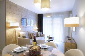 Ein modernes Hotelzimmer mit einer Holzwand, einer Couch, einem Esstisch mit Tellern, Gläsern und einer Flasche.