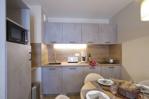 A compact kitchen with a microwave, coffee maker, and a wine bottle on the counter. - Apartment in Éclose with Mountain Views (Huez)