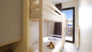 Une chambre d’hôtel avec un lit superposé, une petite table sur laquelle est posé un ours en peluche, et une fenêtre donnant sur une vue sur la montagne.