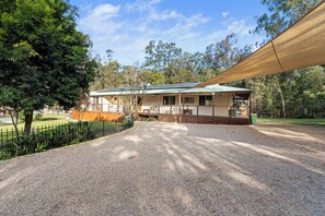 A house with a gravel driveway, a fenced yard, and a large tree to the left.