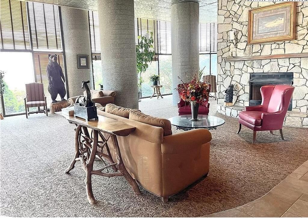 Un hall d’entrée avec une cheminée en pierre, un fauteuil rouge, un canapé marron et une table basse en bois.