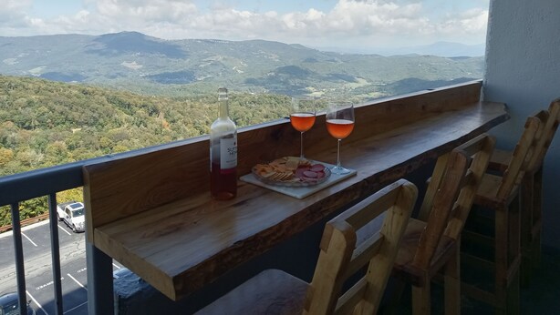 A balcony with a wooden table, two glasses of wine, a bottle of wine, and a plate of snacks. - 2-bedroom condo near Sugar Mountain Resort (Sugar Mountain)