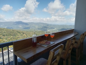 A balcony with a wooden table, two glasses of wine, a bottle of wine, and a plate of snacks. - 2-bedroom condo near Sugar Mountain Resort (Sugar Mountain)
