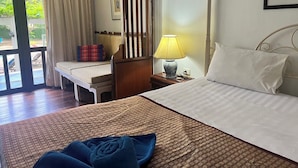 Habitación de hotel con cama, mesita de noche con lámpara, ventana con cortinas y vistas al exterior.