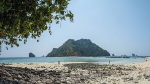 Una playa con primer plano rocoso, agua azul cristalina y dos islas verdes destacadas en la distancia.