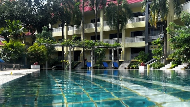 Una piscina con agua cristalina y fondo de azulejos, rodeada por un edificio con balcones y palmeras.
