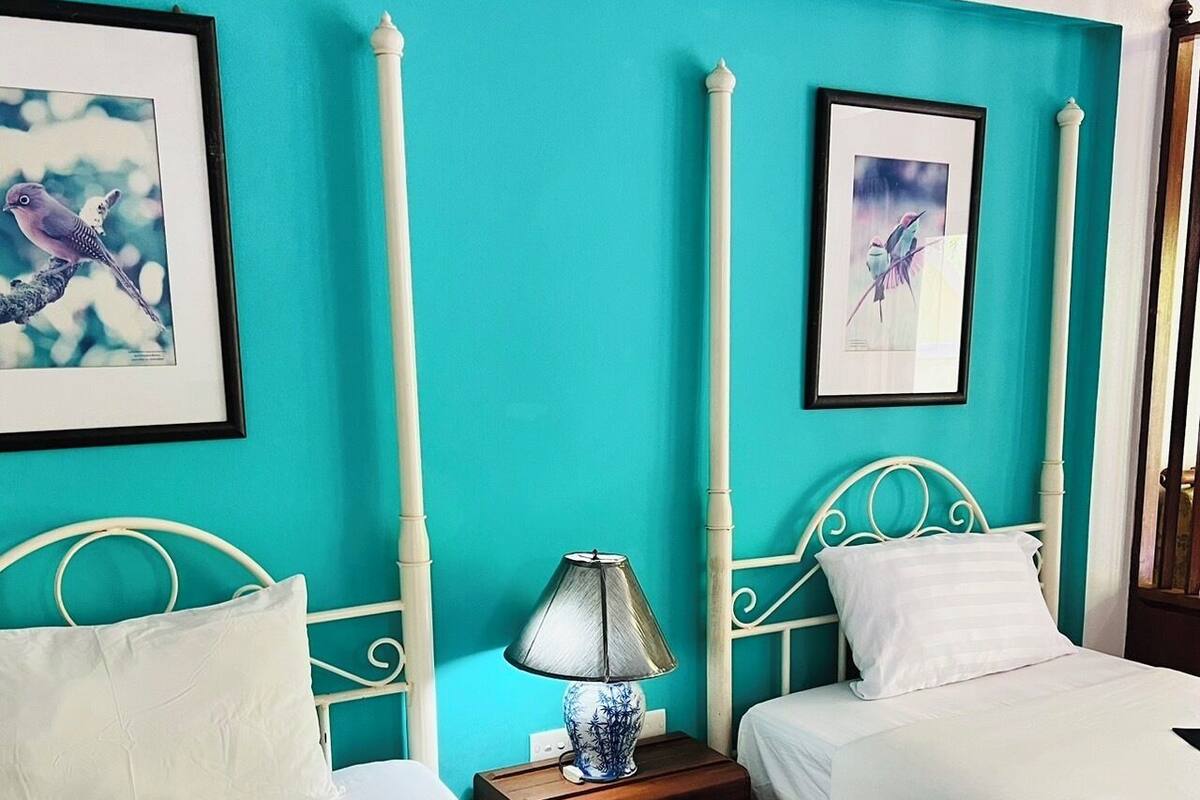 A room with two beds, a nightstand with a lamp, and framed artwork on the walls.