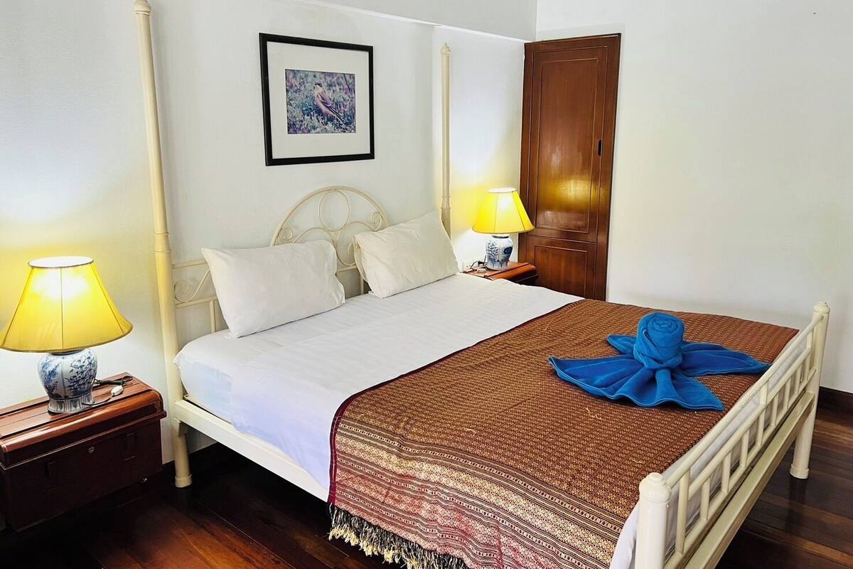 A neatly made bed with a patterned blanket, two bedside lamps, a framed picture on the wall, and a wooden door.