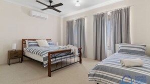 A bedroom with two beds, a ceiling fan, an air conditioning unit, and grey curtains.