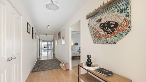 A hallway with a wooden floor, a bench, a wall-mounted artwork, and a door on the left.