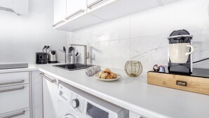 A modern kitchen with white cabinetry, a built-in dishwasher, a coffee maker, and a plate of pastries on the counter. - Cosy Home Chic Milly la Forêt/ Fontainebleau (Milly-la-Forêt)
