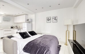 A modern bedroom with a bed, bedside table, and a TV. There is a kitchenette with a microwave, stove, and cabinets.