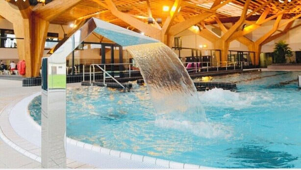 An indoor swimming pool with a waterfall feature, surrounded by wooden beams and a tiled floor. - Cosy Home Chic Milly la Forêt/ Fontainebleau (Milly-la-Forêt)