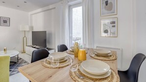 A dining area with a wooden table set for four, a television, and artwork on the walls. - Cosy Home Chic Milly la Forêt/ Fontainebleau (Milly-la-Forêt)