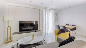 A modern living room with a flat-screen TV, a dining area with a table and chairs, and a sofa. - Cosy Home Chic Milly la Forêt/ Fontainebleau (Milly-la-Forêt)