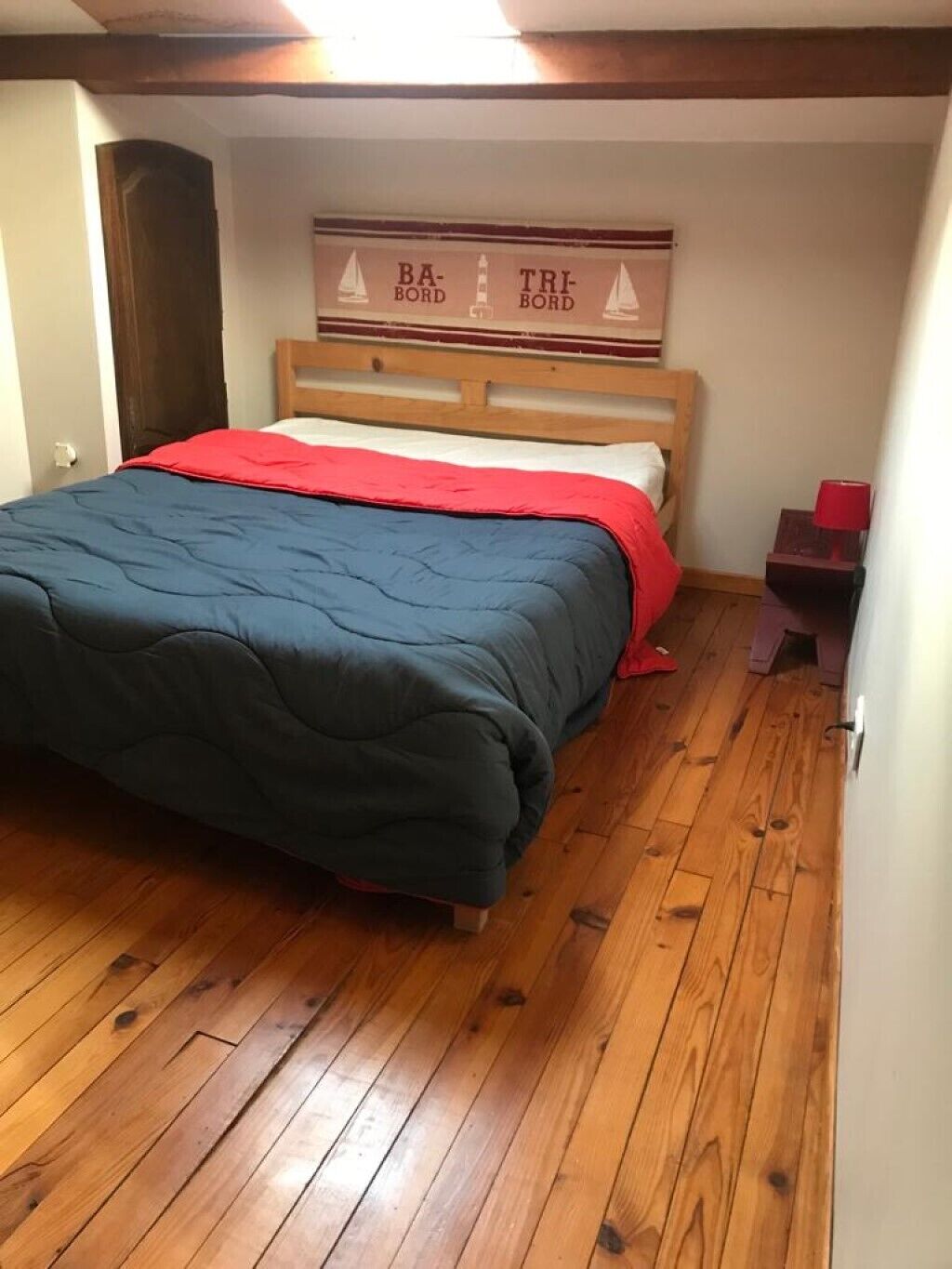 Un dormitorio con suelo de madera, una cama con colcha roja y azul, y un letrero en la pared que dice 'BA-BORD' y 'TRI-BORD'.