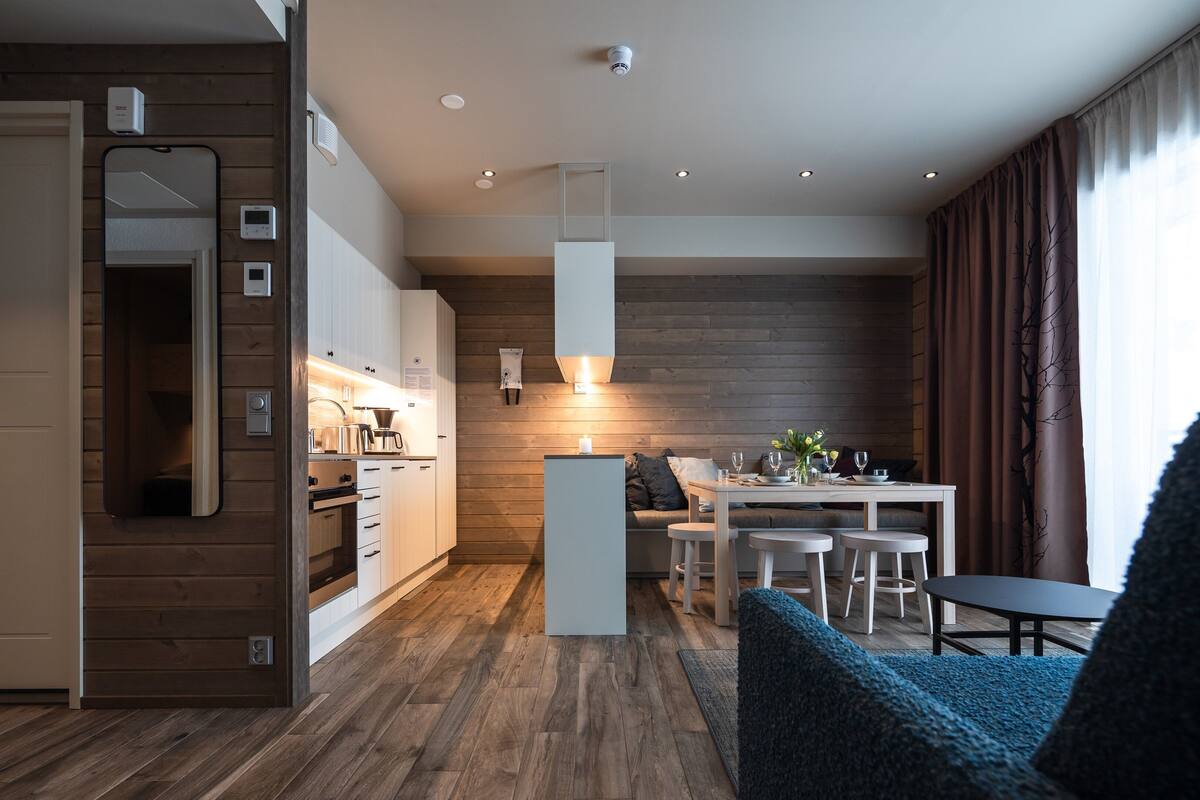 A modern kitchen with wooden accents, a dining area with a table and chairs, and a cozy seating area with a blue sofa.
