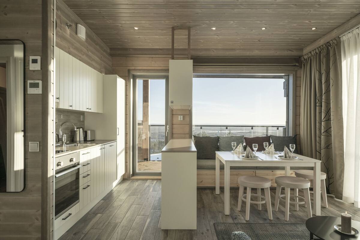 A modern kitchen with white cabinets, a central island, and a dining area with stools.