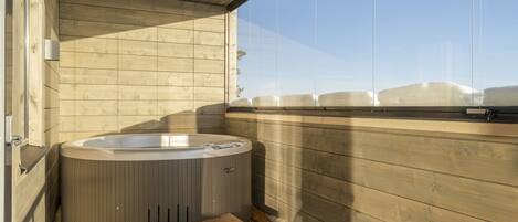 Eine Holzhütte mit Whirlpool, Holzboden und einem Fenster mit Blick auf eine verschneite Landschaft.