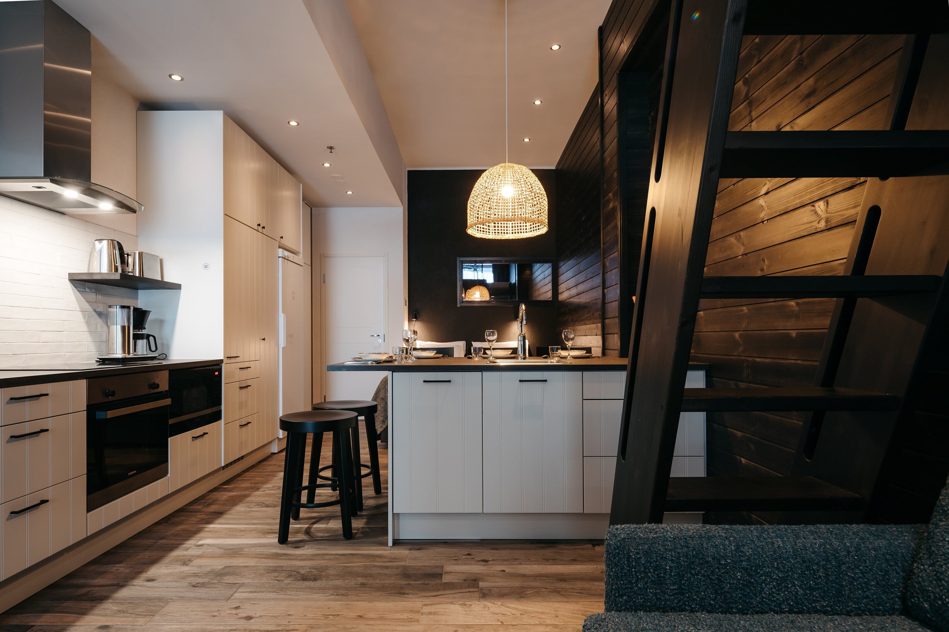 Uma cozinha moderna com armários brancos, piso de madeira e luminária pendente.