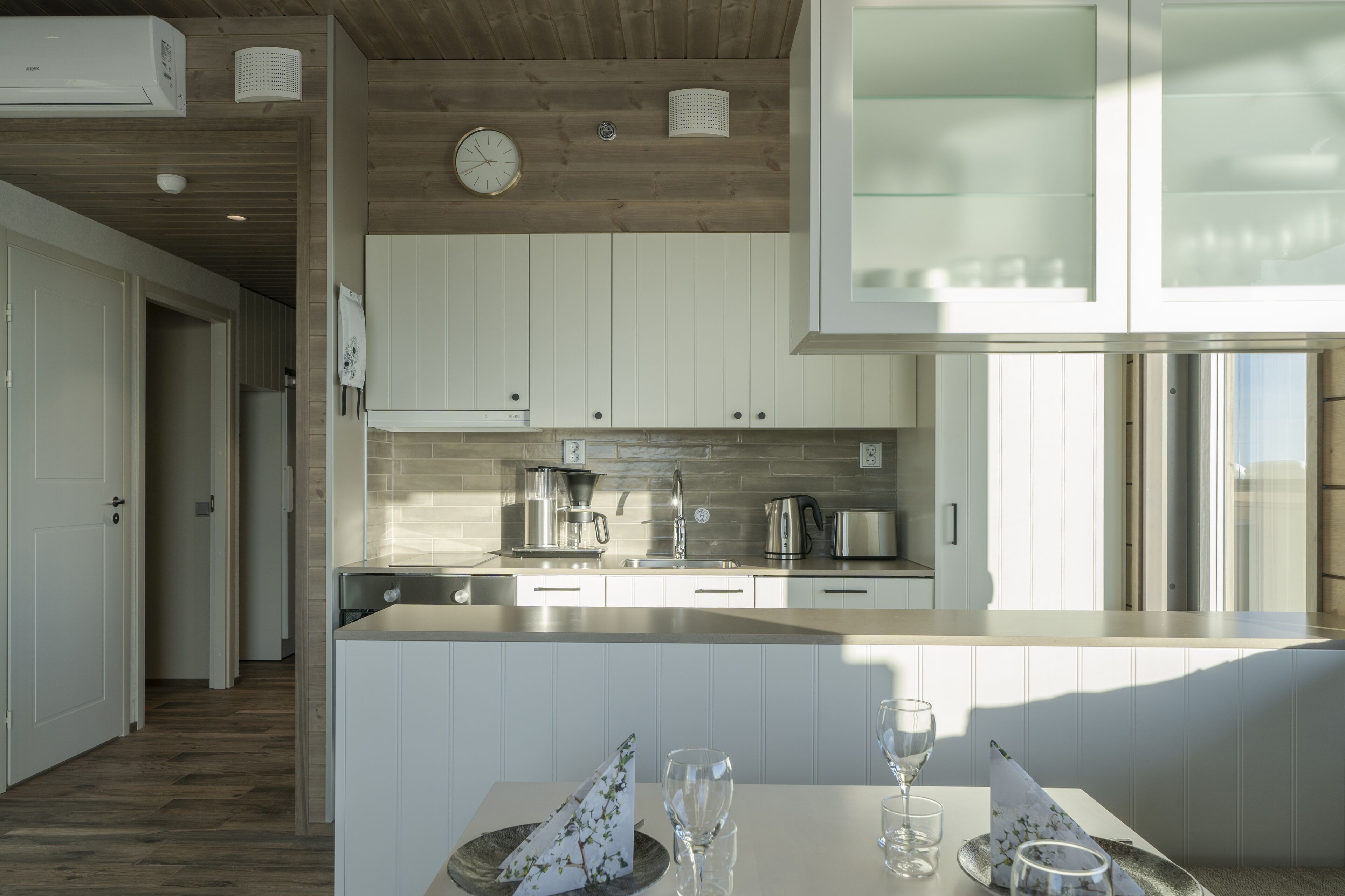 Una cocina moderna con armarios blancos, techo de madera y un ventanal grande.