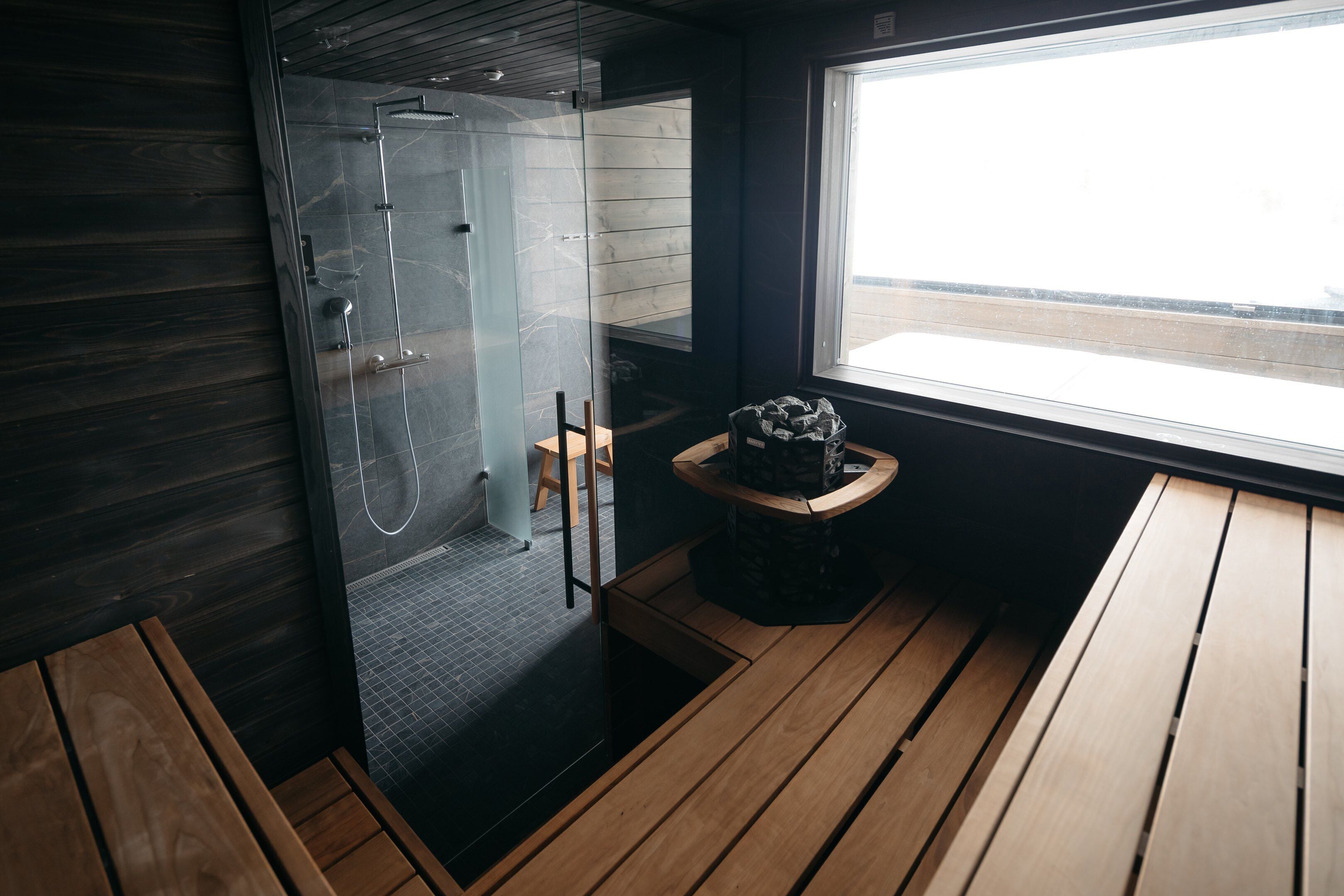 A modern bathroom with a glass-enclosed shower, wooden flooring, and a small table with a decorative item.
