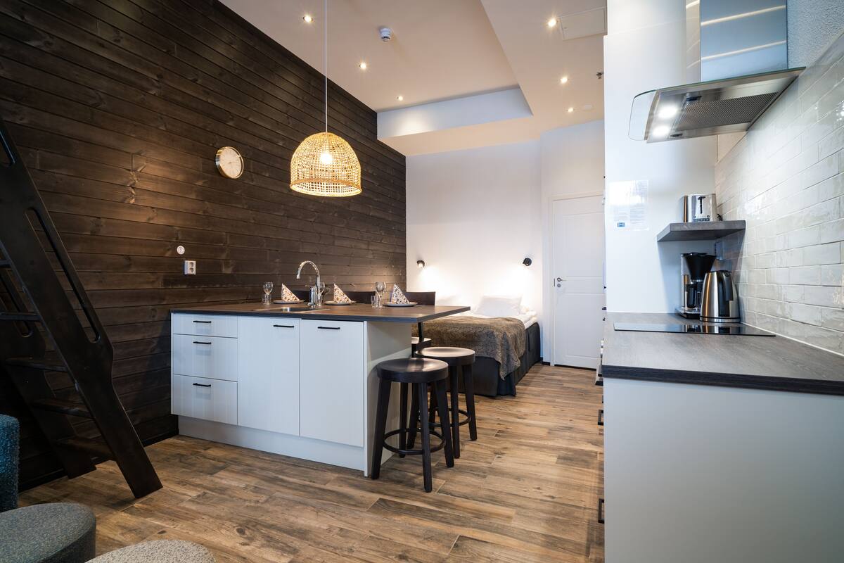 A modern kitchen with a wooden accent wall, a central island with stools, a hanging light fixture, and a built-in stove.