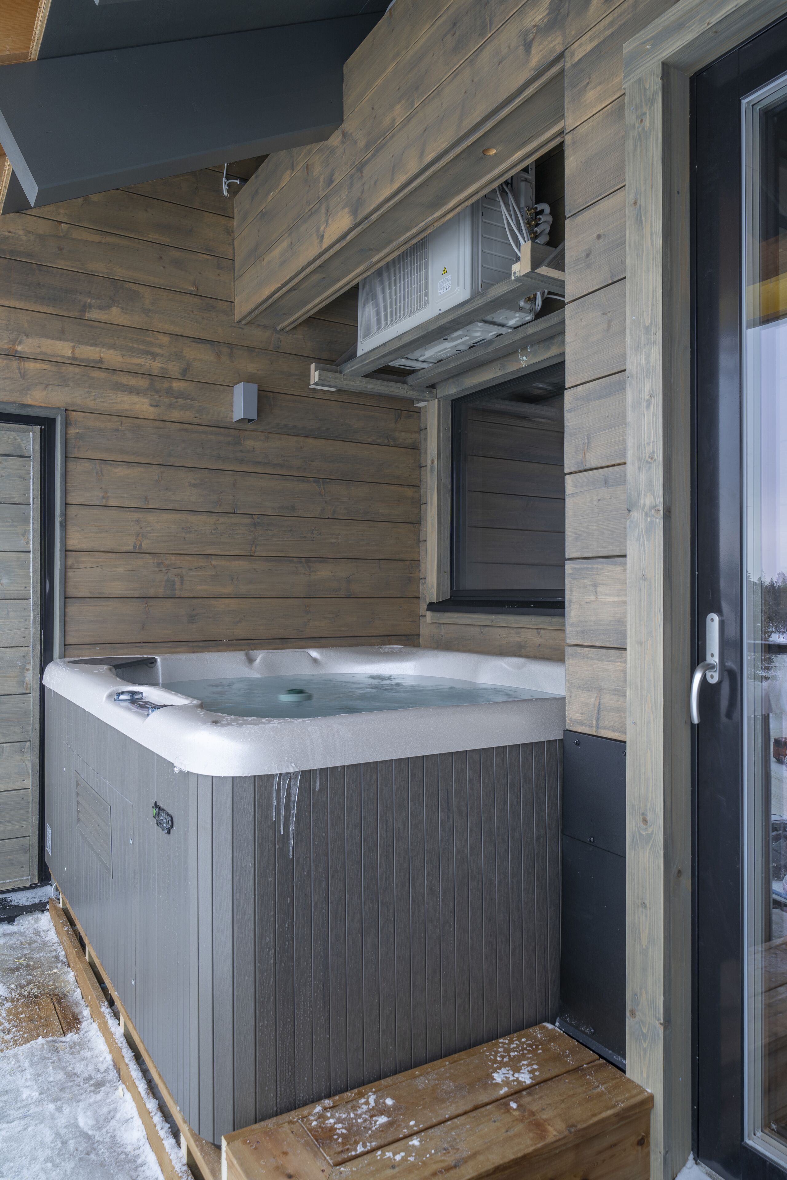 Una cabaña de madera con jacuzzi, una ventana y una puerta.