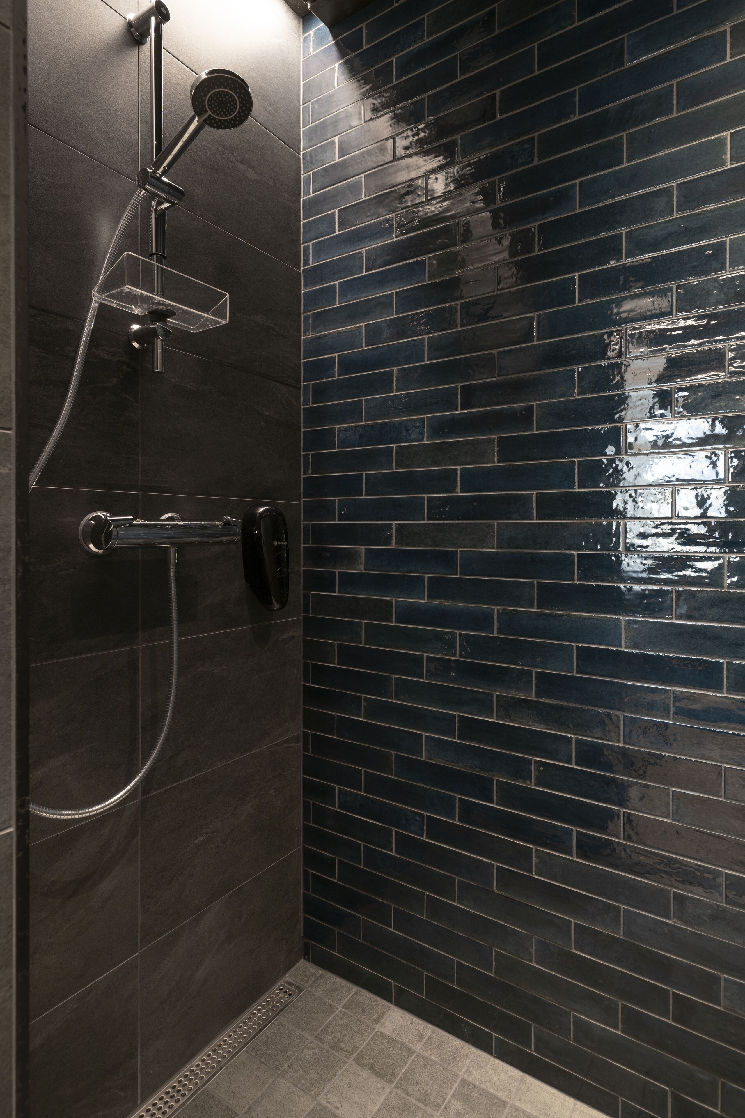 A bathroom with a dark tiled wall, a shower with a handheld showerhead, and a wall-mounted faucet.