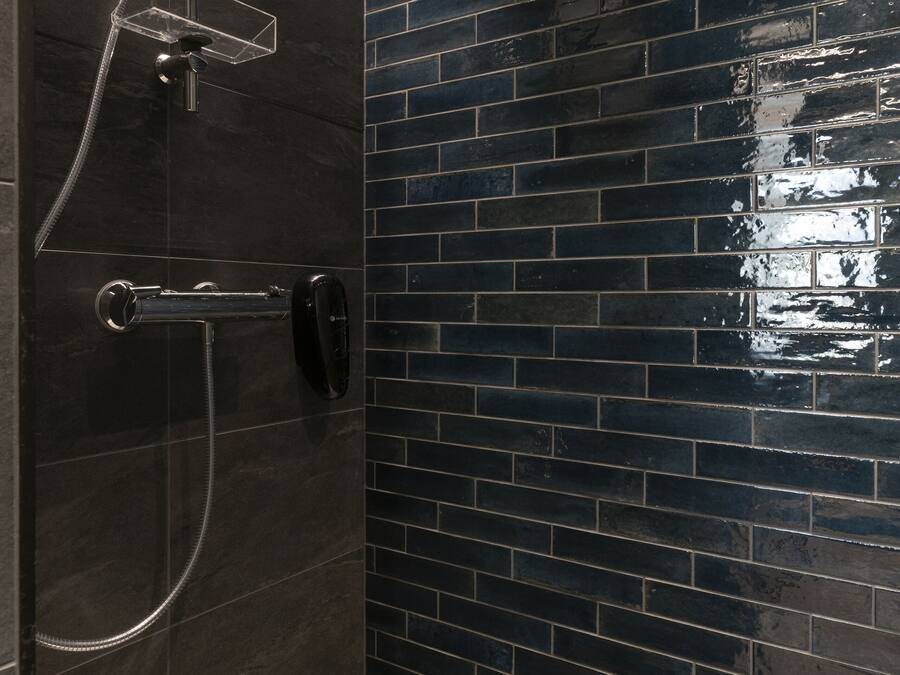Un baño con pared de azulejos oscuros, ducha con cabezal de mano y grifo empotrado.