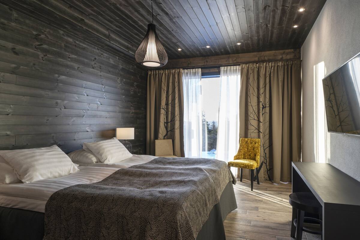 A modern bedroom with a wooden headboard, a large bed with a patterned blanket, a desk, and a chair.