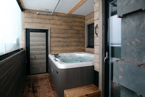 A small, wooden-finished bathroom with a hot tub, a wooden bench, and a glass shower enclosure.