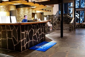 A reception area with a stone wall, a wooden reception desk, and a blue mat with text.