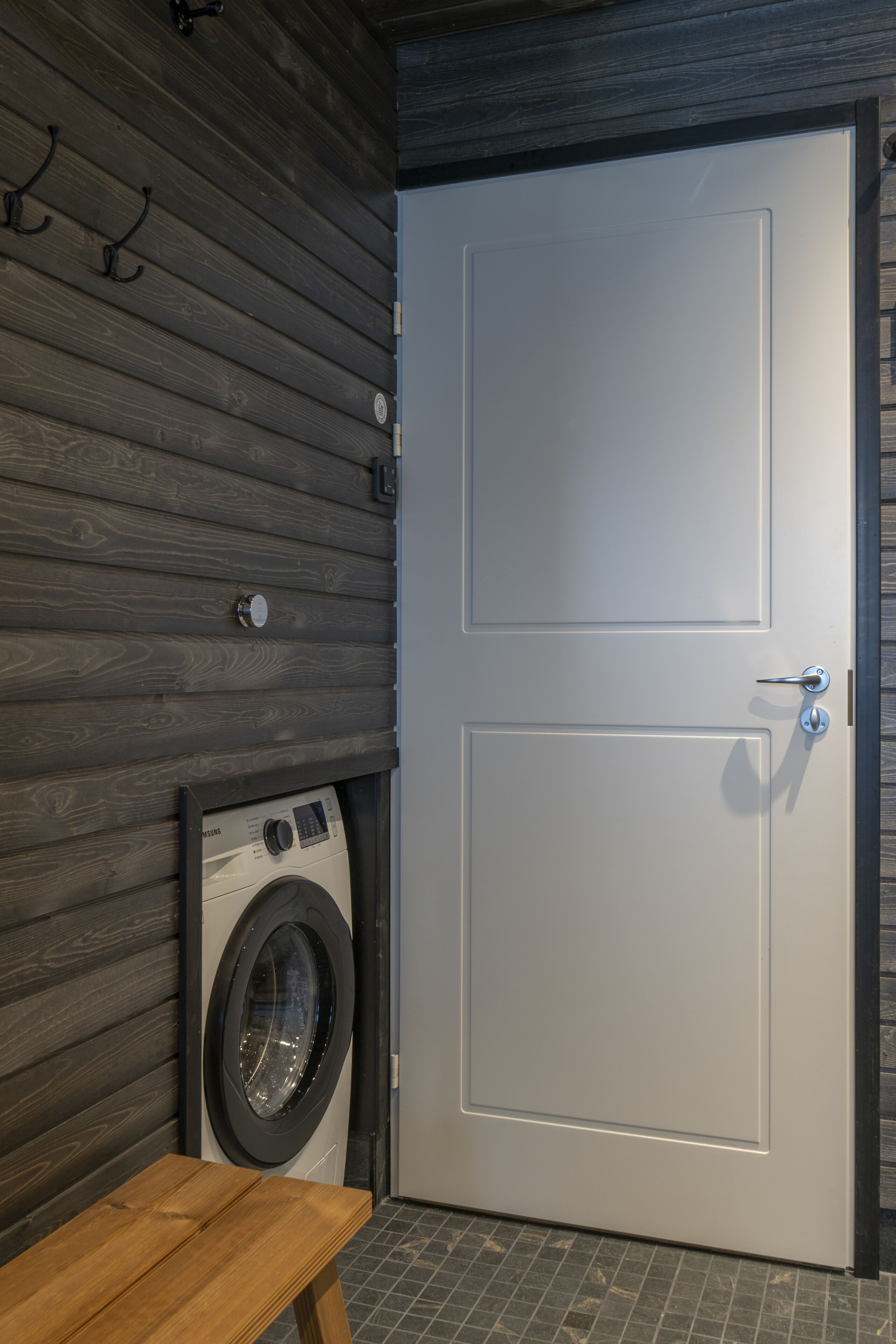 A laundry room with a washing machine, a wooden bench, and a door with a handle.