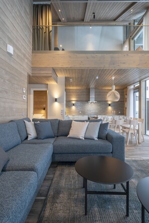A modern living room with a sectional sofa, a round coffee table, and a dining area with a white table and chairs. - Ski-Inn Kultakero (Pyhätunturi)