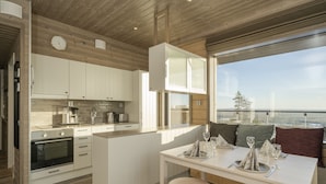 A modern kitchen with white cabinets, a built-in oven, and a dining area with a table set for two. - Ski-Inn Kultakero (Pyhätunturi)