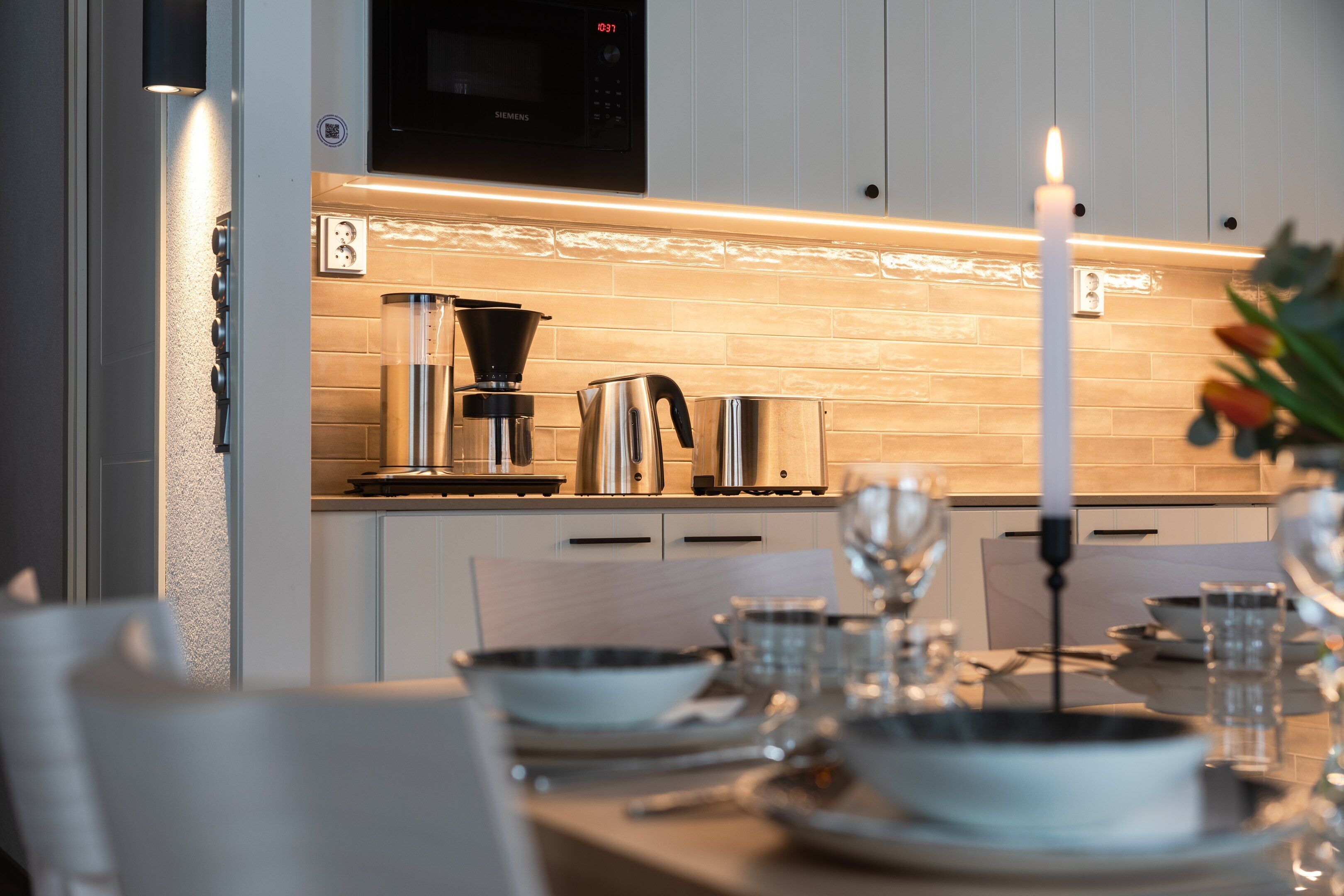 A modern kitchen with a Siemens microwave, a coffee maker, and a lit candle on the table.