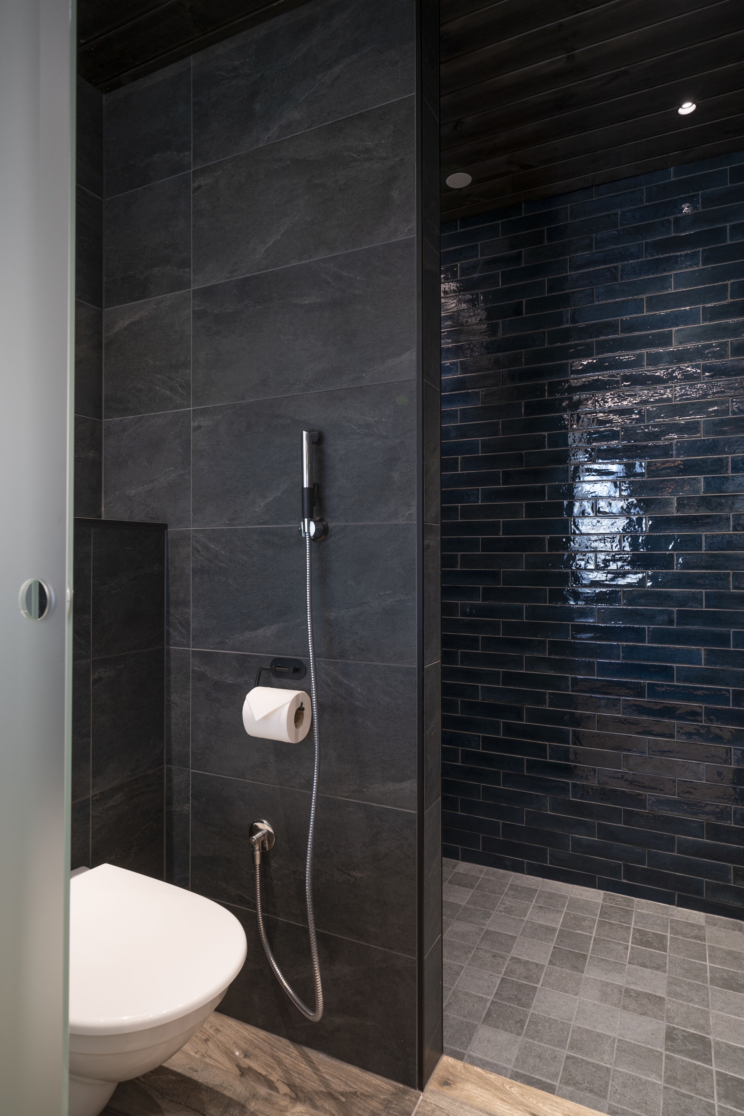 Een moderne badkamer met douche, toilet en donkere betegelde wanden.