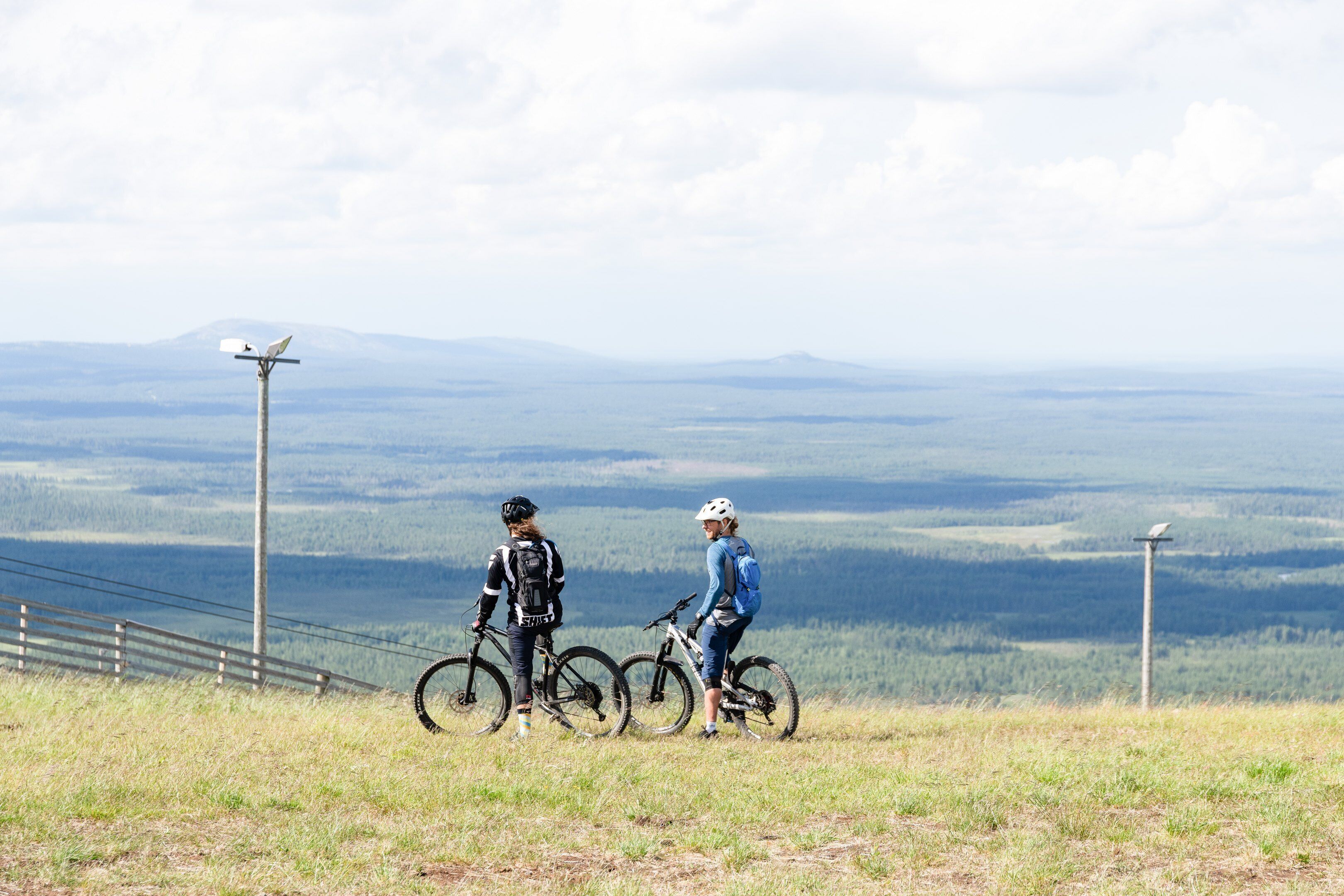 Two people on bicycles on a grassy hill with a view of distant mountains.
