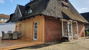 Ein reetgedecktes Häuschen mit einer Holzterrasse und einer Ziegelaußenwand.