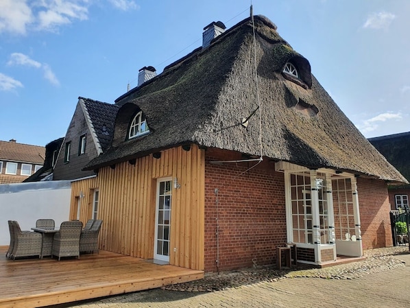 A thatched-roof cottage with a wooden deck and a brick exterior.