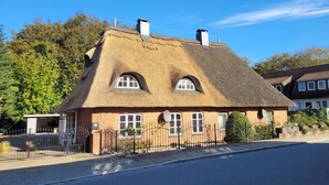 Ein traditionelles Haus mit Strohdach, Backsteinmauern und einem eingezäunten Garten.