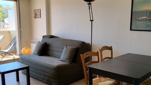 Ett mysigt vardagsrum med en soffa, ett matbord och stolar. Det finns en golvlampa och en inramad tavla på väggen.