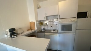 Ett kompakt kök med vita skåp, en inbyggd ugn, en mikrovågsugn, en kaffebryggare och en brödrost.
