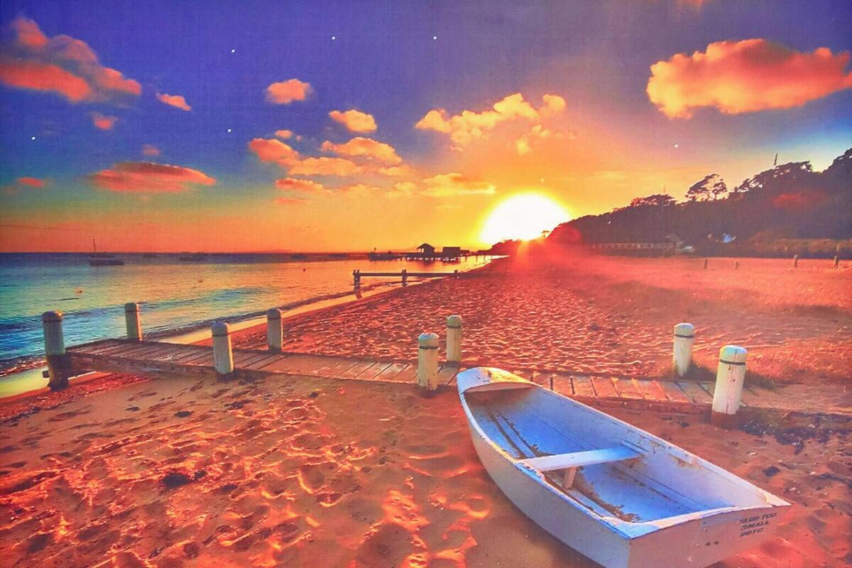 A beach scene with a wooden boat on the sand, a pier, and a sunset in the background.